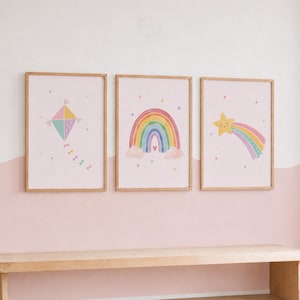 Puede incluir: Tres láminas rectangulares en marcos de madera clara. La lámina de la izquierda muestra una cometa colorida, la central un arcoíris con nubes y un corazón, y la de la derecha una estrella amarilla sonriente con una estela de arcoíris.