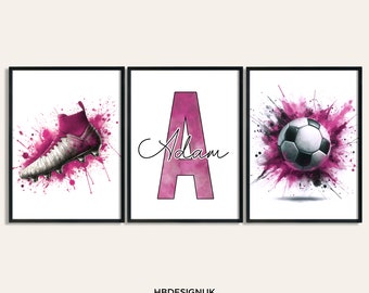 May include: Three pink and black watercolor prints with a soccer theme. The first print features a pink soccer cleat with pink paint splatters. The second print features the letter A in pink with the name Adam written in cursive. The third print features a pink and black paint splatter with a soccer ball in the center.