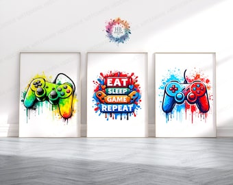 Puede incluir: Tres impresiones enmarcadas con un tema de juegos. La impresión de la izquierda presenta un mando de videojuego verde y amarillo con salpicaduras de pintura de colores. La impresión del medio tiene el texto "Eat Sleep Game Repeat" en letras de colores con salpicaduras de pintura. La impresión de la derecha presenta un mando de videojuego rojo y azul con salpicaduras de pintura de colores.
