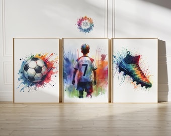 May include: Set of three framed watercolor prints featuring soccer themes. One print shows a soccer ball, another a soccer player with the name "ADAM" and the number "7" on the jersey, and the third a soccer cleat. Each print has colorful paint splatter effects.