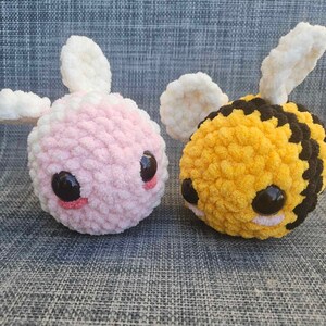 May include: Two crocheted stuffed animals, one pink with white wings and the other yellow and black with white wings, resembling a bee.
