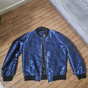 May include: A blue bomber jacket with a paisley pattern and a gold zipper. The jacket has a black ribbed collar, cuffs, and waistband.