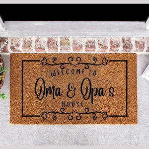 May include: A brown coir doormat with black text that reads "Welcome to Oma & Opa's House" with a decorative border of hearts and swirls.