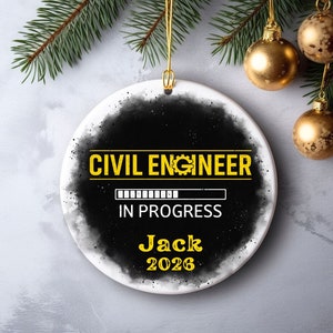 May include: A round white ceramic ornament with the text "CIVIL ENGINEER IN PROGRESS" in yellow. The name "Jack" and the year "2026" are also displayed. The ornament has a black and gray speckled border and is hanging from a gold string.