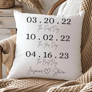 May include: White throw pillow with black text that reads "03.20.22 The First Day 10.02.22 The Yes Day 04.16.23 The Best Day Jasmine Steven".