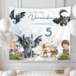 May include: A white birthday banner featuring cartoon dragons and Viking characters. The banner reads "Our little viking Veronika is celebrating birthday 5". White balloons are visible on the left and right sides of the banner.