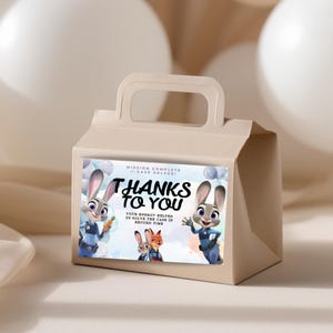 Puede incluir: Una caja de regalo beige con asa, con una pegatina colorida con el texto "THANKS TO YOU". La pegatina incluye im&aacute;genes de dibujos animados de conejos y zorros, con la frase "MISSION COMPLETE - CASE SOLVED!" y otro texto.