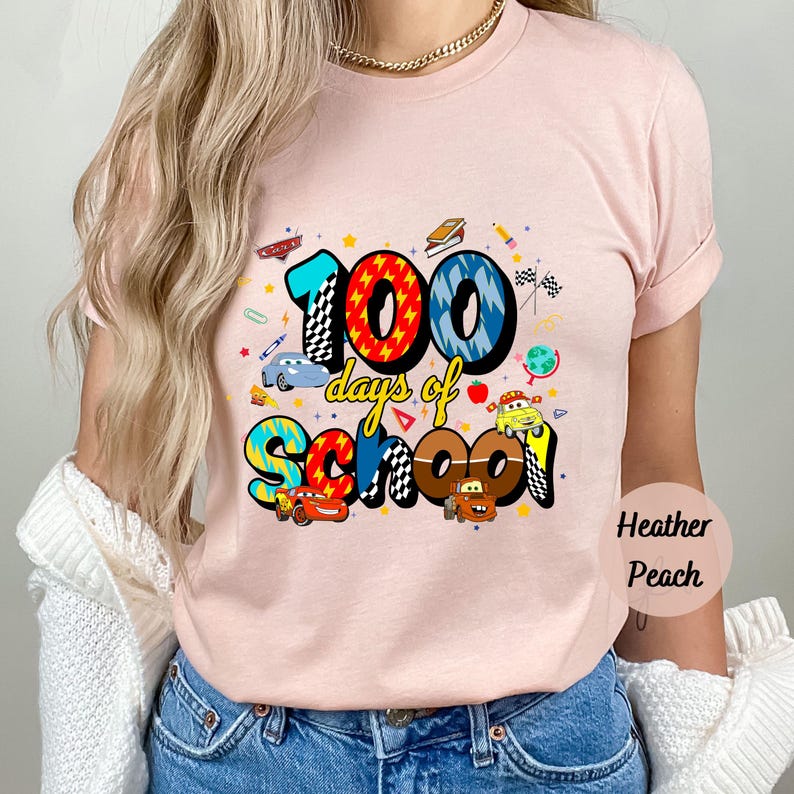 A woman wearing a pink t-shirt with a graphic design that says "100 days of school" and features various cartoon cars and other school-related elements.