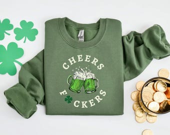 May include: Green sweatshirt with the text "CHEERS F*CKERS" in white lettering. The sweatshirt features a graphic of two green beer mugs clinking together.