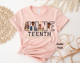 May include: A heather peach short-sleeve t-shirt featuring the text "JUNE TEENTH Freedom Day" in black and olive green. The graphic includes stylized illustrations of four Black individuals integrated into the letters of the word "JUNE".