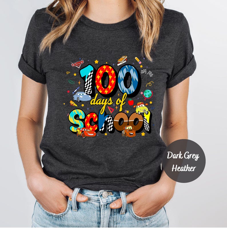 A person wearing a black t-shirt with a colorful graphic design that says "100 days of school" and features various cartoon characters and objects related to education.