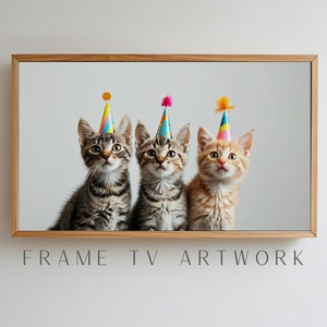 以下が含まれることがあります： カラフルなパーティーハットをかぶった子猫が3匹います。子猫たちは一列に並んでカメラを見上げています。背景は白い壁です。