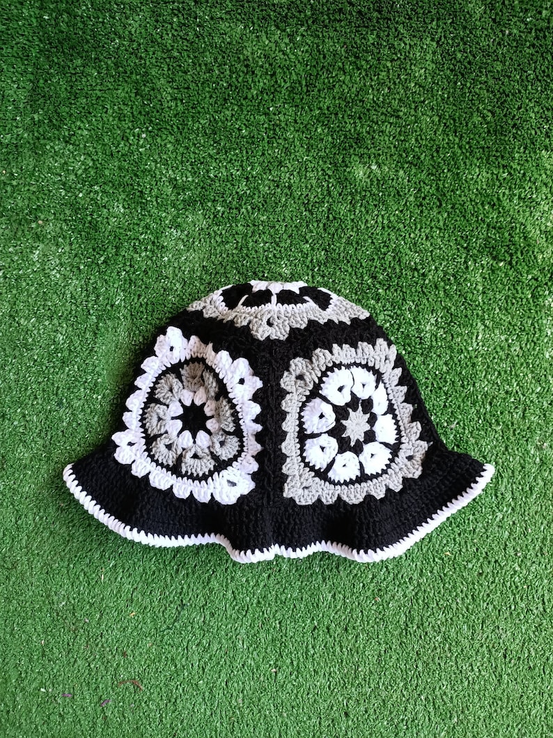 Pu&ograve; includere: Un cappello a secchiello in crochet nero e bianco con un motivo geometrico. Il cappello ha un'ampia tesa ed &egrave; realizzato con una combinazione di filato nero, bianco e grigio.