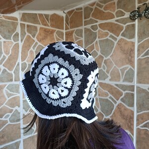 Pu&ograve; includere: Un cappello a secchiello all'uncinetto nero, bianco e grigio con un bordo a scalare.