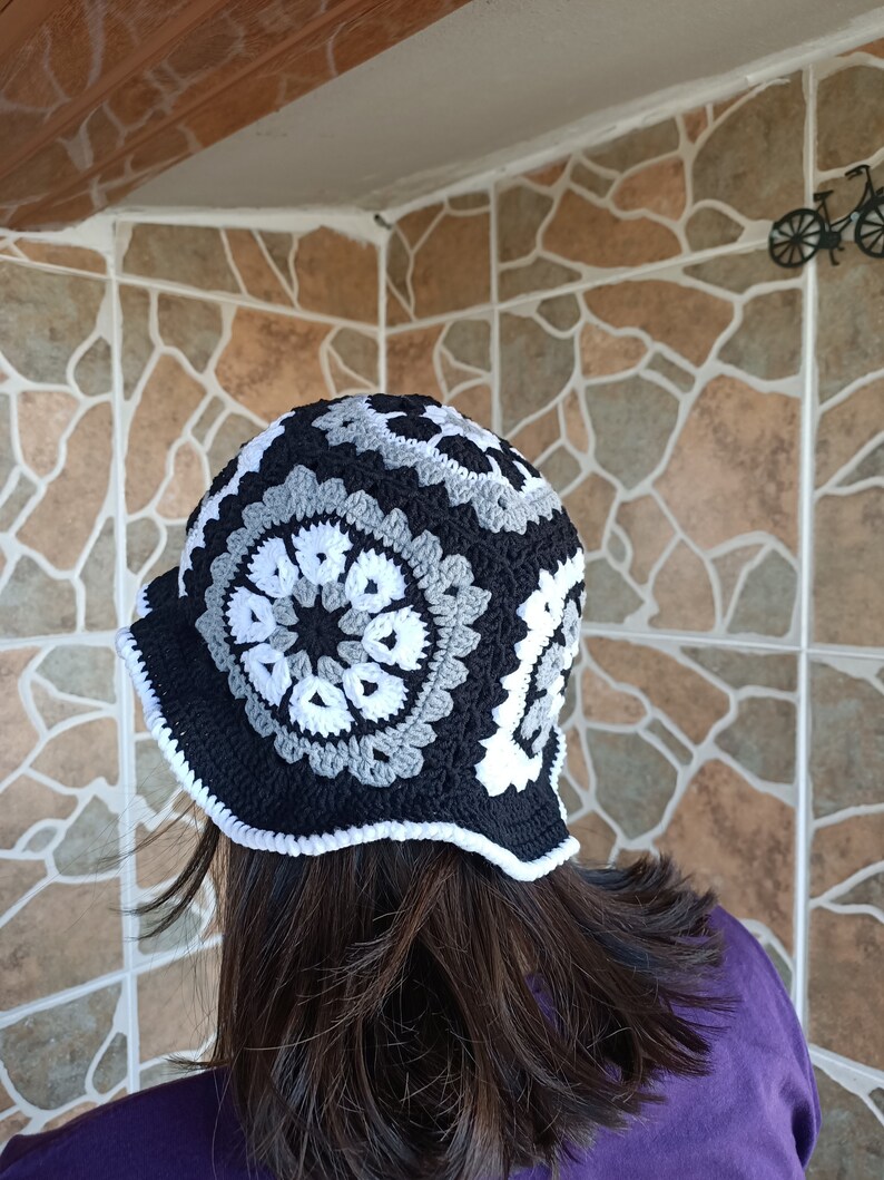 Pu&ograve; includere: Un cappello a secchiello all'uncinetto nero, bianco e grigio con un bordo a scalare.