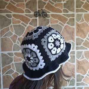 Pu&ograve; includere: Un cappello a secchiello in crochet nero e bianco con un bordo a scalare. Il cappello &egrave; realizzato con un motivo di cerchi ripetuti.