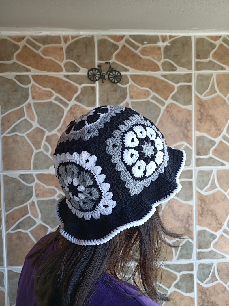 Pu&ograve; includere: Un cappello a secchiello in crochet nero e bianco con un bordo a scalare. Il cappello &egrave; realizzato con un motivo di cerchi ripetuti.