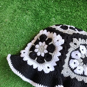 Pu&ograve; includere: Un cappello a secchiello lavorato a uncinetto nero, bianco e grigio con un bordo a scalare.