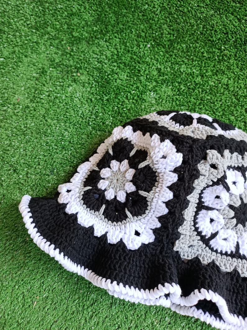 Pu&ograve; includere: Un cappello a secchiello lavorato a uncinetto nero, bianco e grigio con un bordo a scalare.