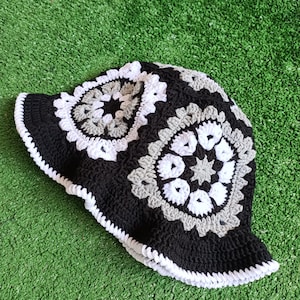 Pu&ograve; includere: Un cappello a secchiello in crochet nero con motivi di fiori in crochet bianco e grigio.