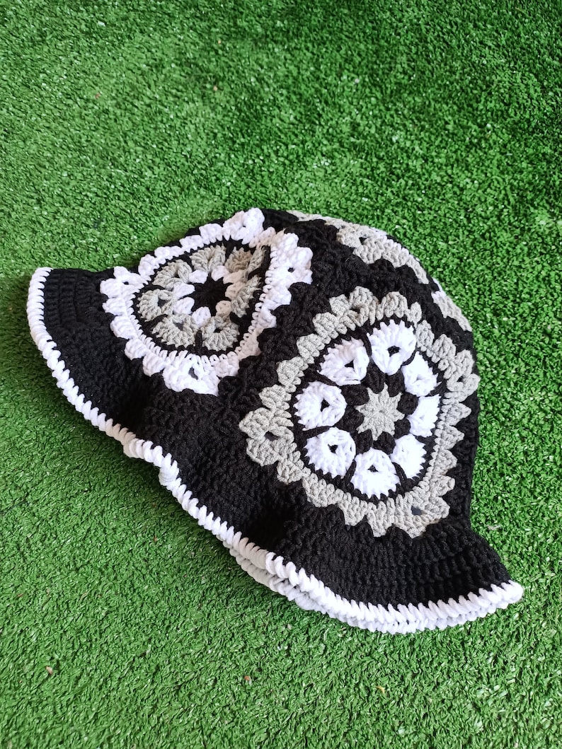 Pu&ograve; includere: Un cappello a secchiello in crochet nero con motivi di fiori in crochet bianco e grigio.