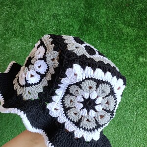 Pu&ograve; includere: Un cappello a secchiello in crochet bianco e nero con un bordo a scalare. Il cappello presenta un motivo ripetuto di cerchi con un centro grigio.