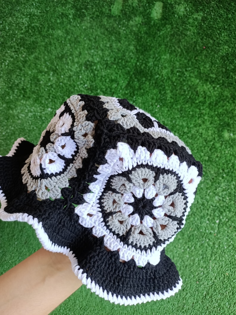 Pu&ograve; includere: Un cappello a secchiello in crochet bianco e nero con un bordo a scalare. Il cappello presenta un motivo ripetuto di cerchi con un centro grigio.