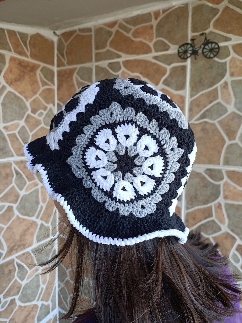 Pu&ograve; includere: Un cappello a secchiello in crochet nero, bianco e grigio con un bordo in crochet bianco.