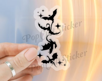 Peut inclure: Un autocollant transparent avec un motif de quatre dragons noirs volant en ligne verticale. Les dragons sont en silhouette sur un fond blanc. Il y a de petites étoiles blanches éparpillées autour des dragons.