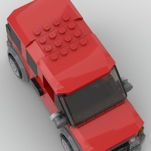 K&ouml;nnte beinhalten: Ein rotes Spielzeugauto mit einer schwarzen Windschutzscheibe und grauen R&auml;dern. Das Auto hat ein abnehmbares Dach mit einem Muster aus roten LEGO-Steinen.