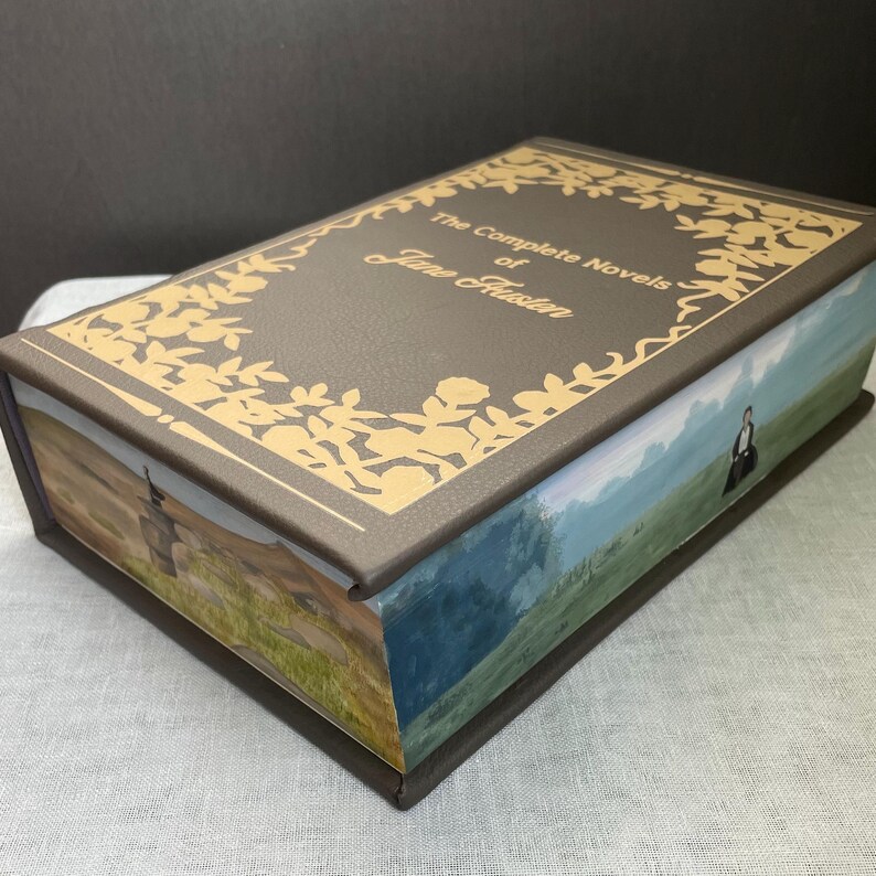 May include: A gray box with a gold embossed design and the text "The Complete Novels of Jane Austen". The box has a landscape scene on the side.