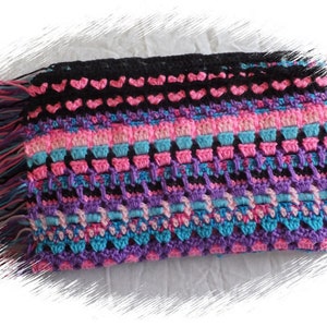 Könnte beinhalten: Eine bunte Häkeldecke mit Fransenrand. Die Decke ist in verschiedenen Farben gehalten, darunter Pink, Lila, Blau und Schwarz. Die Decke ist mit verschiedenen Maschen gearbeitet, darunter Herzen und Quadrate.