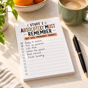 May include: A white notepad with the text STUFF I ABSOLUTELY MUST REMEMBER BUT WILL PROBABLY FORGET printed in colorful letters. The page features a checklist with lines and empty boxes, including handwritten entries for emails, groceries, and laundry.