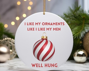 May include: White ceramic Christmas ornament with the text "I LIKE MY ORNAMENTS LIKE I LIKE MY MEN WELL HUNG." The ornament features a red and white striped bauble design. A gold string is attached for hanging.