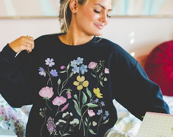 Könnte beinhalten: Ein schwarzer Pullover mit einem Blumendruck mit rosa, gelben, blauen und violetten Blumen. Der Pullover hat eine lockere Passform und einen Rundhalsausschnitt.