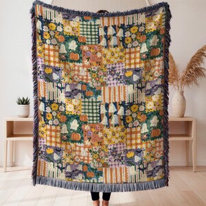May include: A woven throw blanket featuring a patchwork design of various patterns including orange and white stripes, green and white plaid, yellow flowers, pumpkins, and white ghosts, finished with a dark blue fringed edge on all sides.