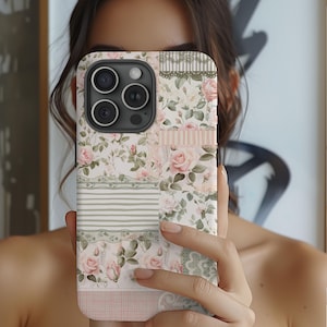 May include: A phone case with a floral pattern featuring pink roses, green leaves, and white lace accents. The case has a patchwork design with different patterns and textures.