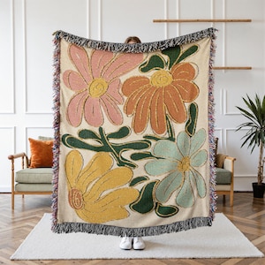 Boho flower woven blanket with vintage large floral design in earthy tones.  Showns 4 large flowers in retro style design in earth tone colors.  Perfect as  tapestry, throw for sofa, bed, or wall hanging,  Beige color shown here being held up by a person.