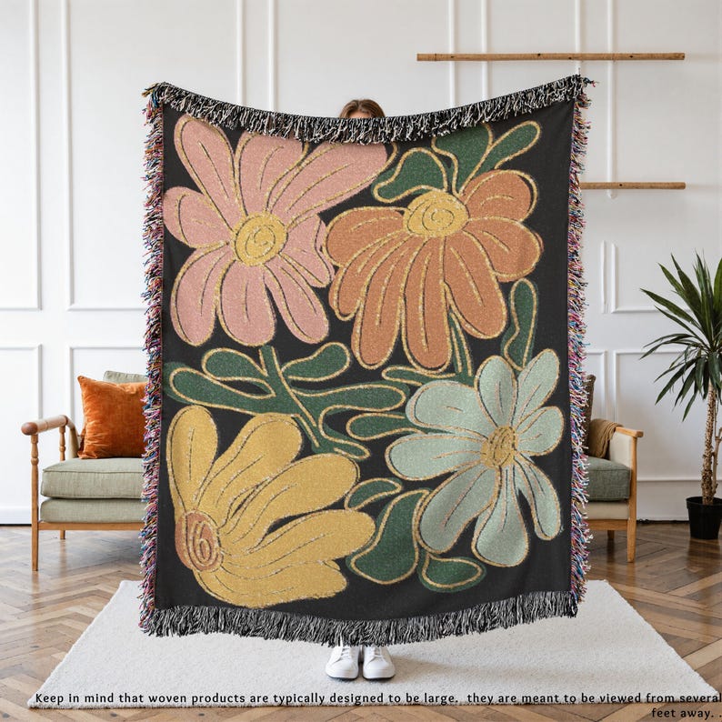 Boho flower woven blanket with vintage large floral design in earthy tones.  Showns 4 large flowers in retro style design in earth tone colors.  Perfect as  tapestry, throw for sofa, bed, or wall hanging,  Black color shown here being held up by a person.
