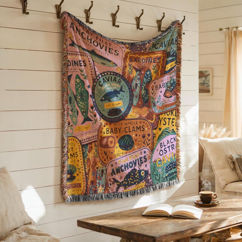Vintage-style woven tapestry blanket featuring colorful sardine, anchovy, caviar, and clam labels in a collage design.  Blanket is being shown as a wall tapestry