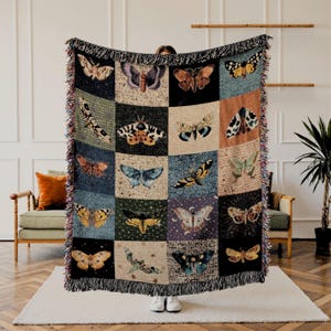 May include: A woven tapestry throw blanket with a patchwork design featuring colorful butterflies and moths. The blanket has a fringed edge and is made of a soft, textured fabric.