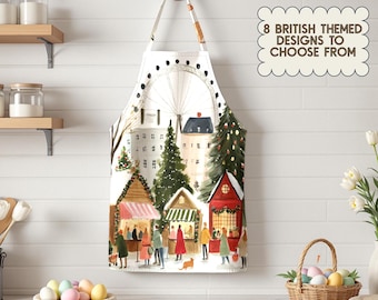 Op de afbeelding: Witte schort met een aquarel illustratie van een Britse kerstmarkt, inclusief een reuzenrad en feestelijke kraampjes. De schort heeft een crèmekleurige band en de tekst "8 BRITISH THEMED DESIGNS TO CHOOSE FROM".