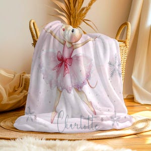 May include: A pink and white blanket featuring a watercolor illustration of a ballerina mouse in a pink tutu and bow. The blanket has snowflake accents and the name "Charlotte" in cursive script.