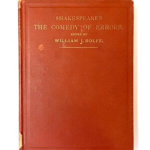 May include: A red hardcover book with gold lettering on the front cover. The title is "Shakespeare's The Comedy of Errors" and the book is edited by "William J. Rolfe."