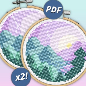 May include: Two circular wooden embroidery hoops containing cross-stitch patterns of a mountain landscape at sunset. The designs feature shades of purple, blue, and green with a yellow sun. A blue circular icon with the text PDF and another with x2!.