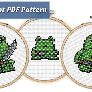 May include: Three cross-stitch patterns featuring green frogs with black eyes. The frogs are holding knives and are in different poses. The patterns are in embroidery hoops.
