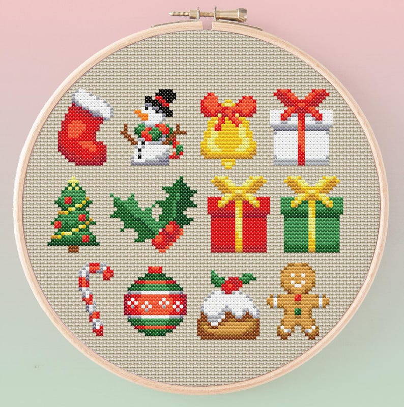 May include: A cross-stitch embroidery hoop featuring various Christmas-themed icons. The design includes a red stocking, snowman, bell, wrapped gifts, Christmas tree, holly, candy cane, ornament, pudding, and gingerbread man.