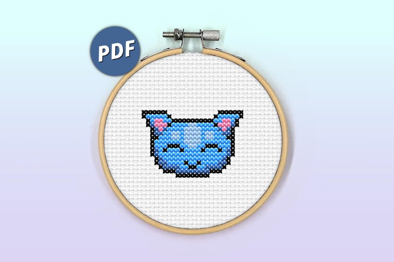 May include: A cross-stitch pattern of a blue cat with pink ears and a white face. The cat is stitched on white Aida cloth and framed in a wooden hoop.