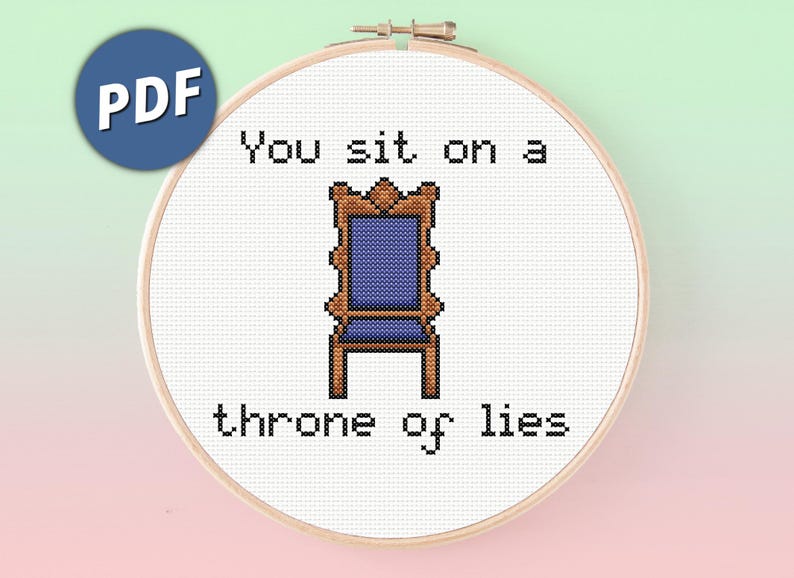 May include: A cross stitch pattern in a wooden embroidery hoop featuring a pixelated blue and brown chair centered between the black text You sit on a throne of lies. The design is displayed on a white fabric background with a blue PDF icon.