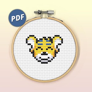 May include: A cross-stitch pattern of a yellow tiger face with blue eyes, in a wooden embroidery hoop.